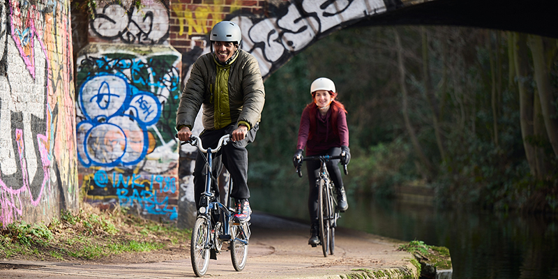 A man and a woman cycling along a canal path smiling