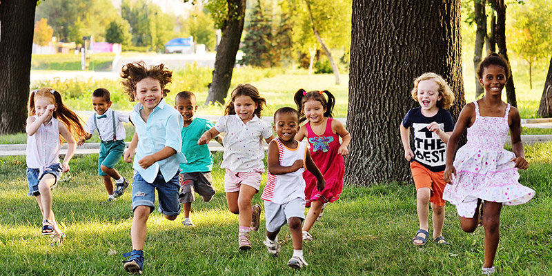 a group of preschoolers running on the grass in the Park.