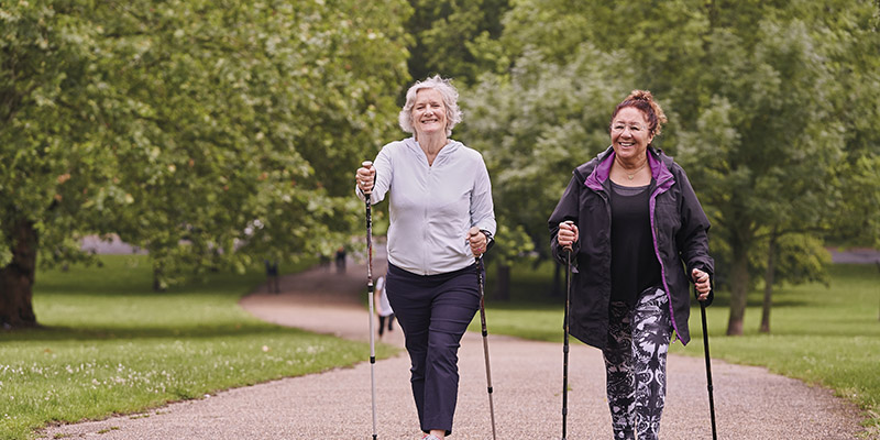 Two women walking with nordic walking sticks through a park