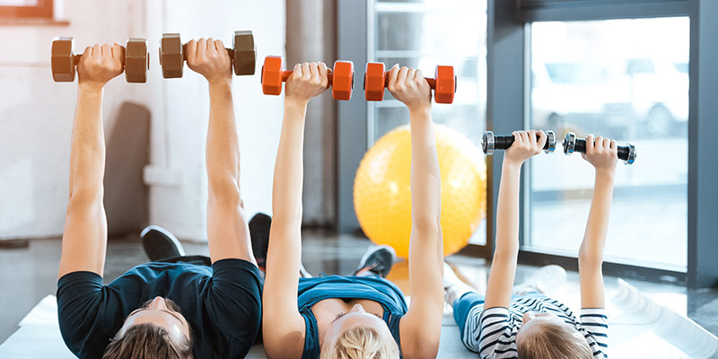 Happy family exercising with dumbbells at fitness studio