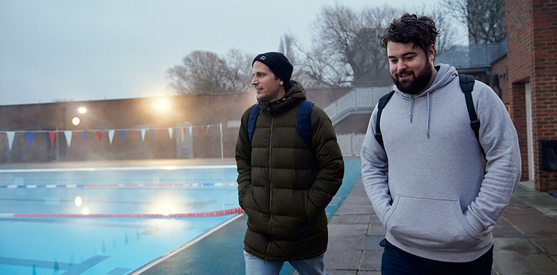 Two young men walking together beside an outdoor swimming pool