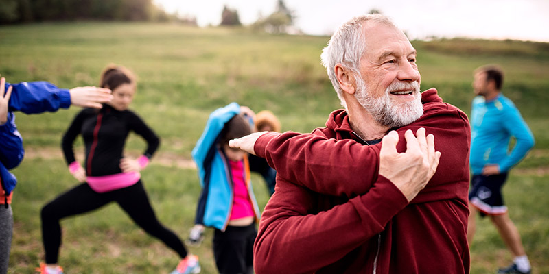 Large group older people doing exercise in nature, stretching.