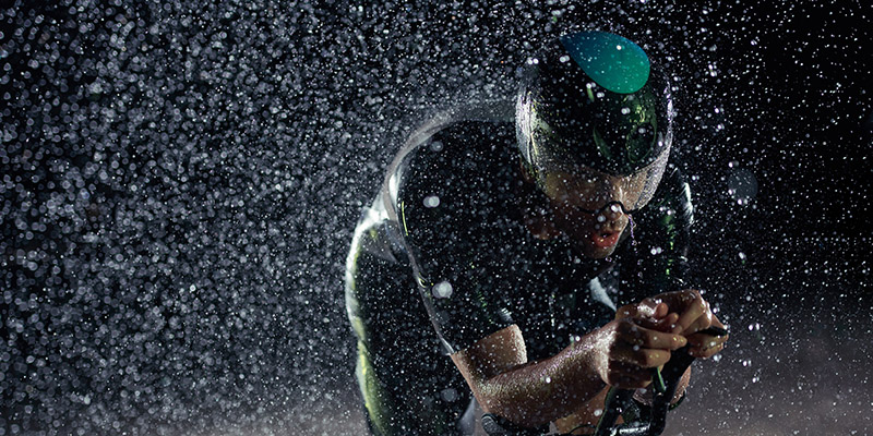 triathlon athlete riding bike fast on rainy night