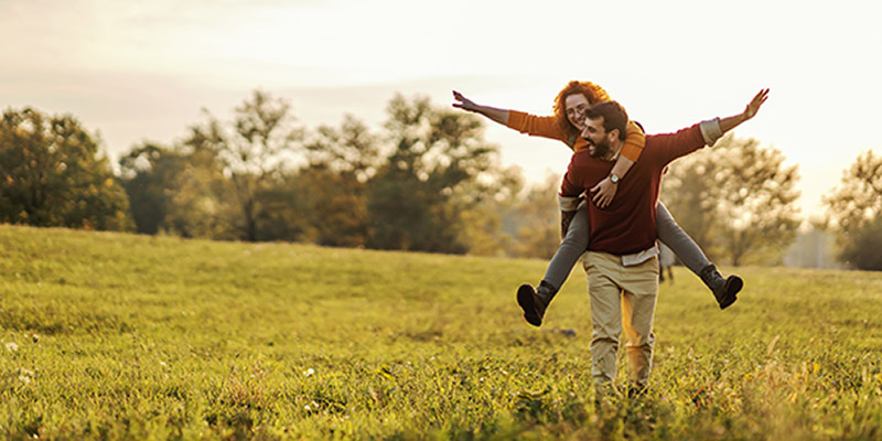 Young happy playful couple in love having piggyback ride in nature